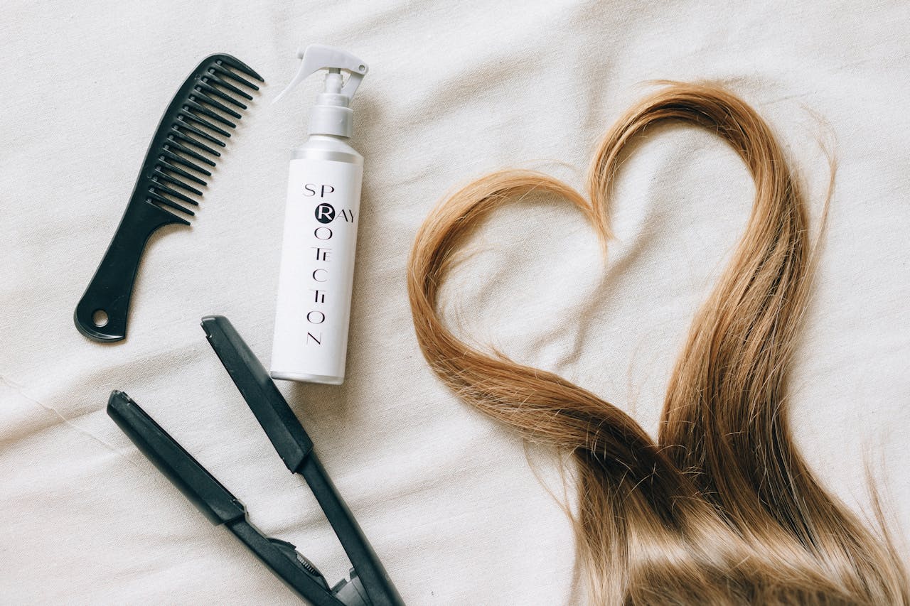 services-01 Flat lay of hair styling tools on a bedsheet with heart-shaped hair strand.