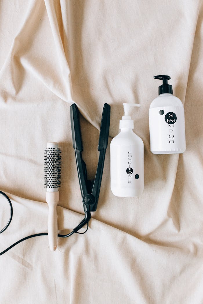 services-03 Flat lay of hairbrush, hair iron, and shampoo bottles on fabric background.
