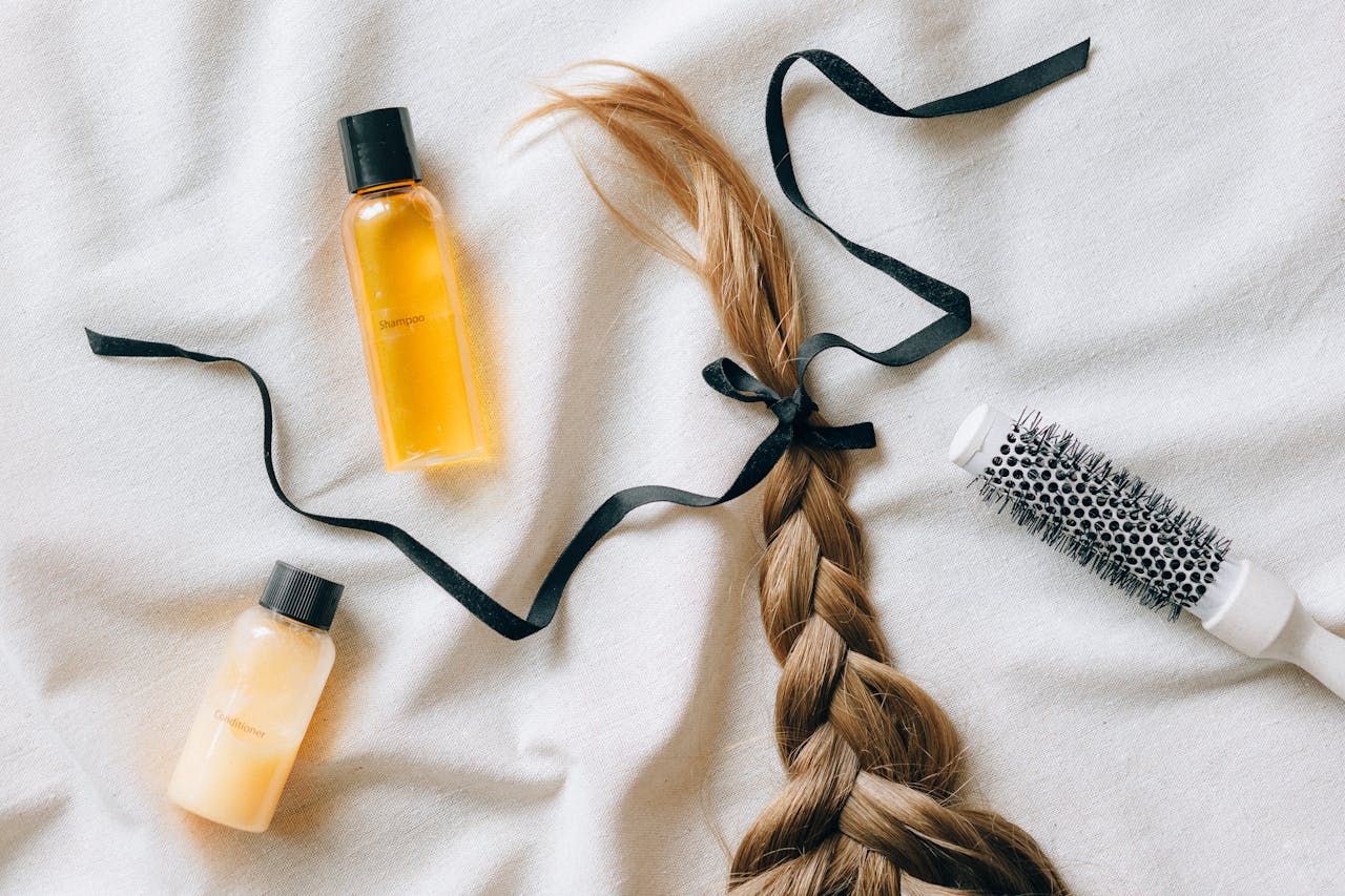 gallery-6 Flat lay of braided hair with shampoo bottles and brush on white fabric, conveying beauty and haircare themes.