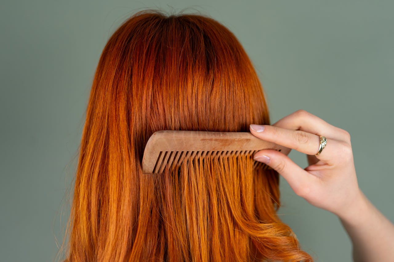 hero-img-02 Close-up of a womans red hair being combed with a wooden comb, capturing the smooth texture.